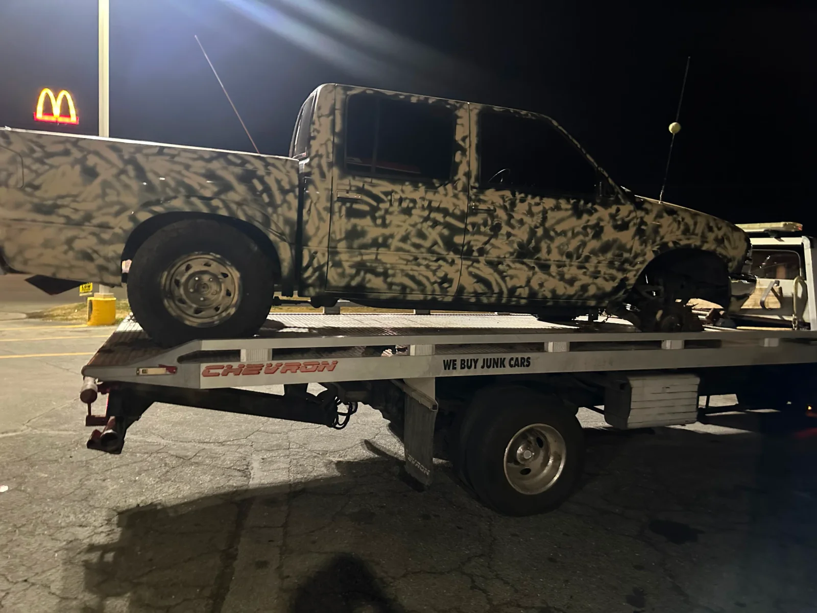 Camouflage-painted pickup secured on a flatbed at night